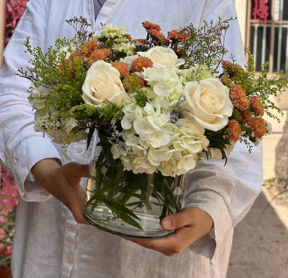 Seasonal floral vase with ivory roses, rust-orange chrysanthemums, and wild greens